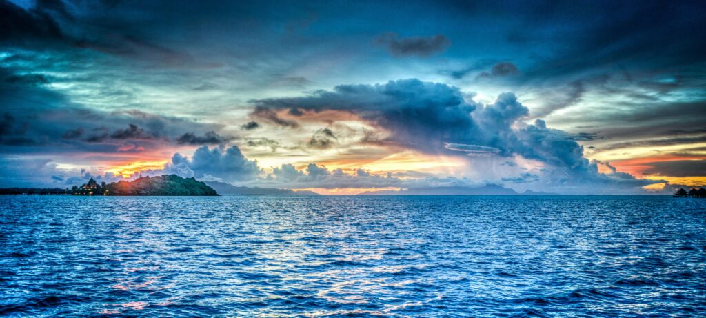 Vibrant sunset over tropical ocean with dramatic clouds and distant island.