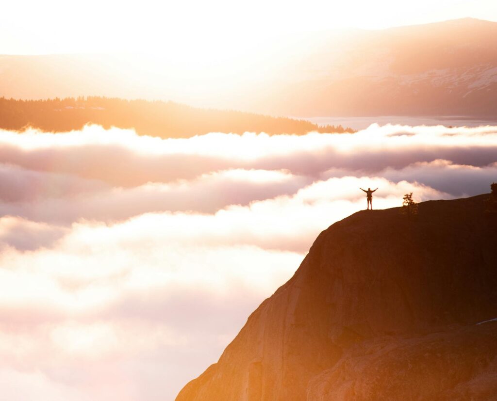 Silhouette of a person standing triumphant on a mountain cliff amidst the breathtaking morning clouds.