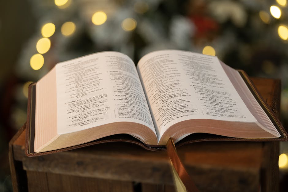 Open Bible resting on wooden surface with blurred festive background lights.