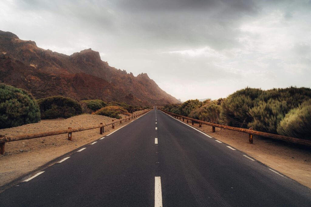 A picturesque road leads through the mountainous landscape of Tenerife, Spain under a cloudy sky.